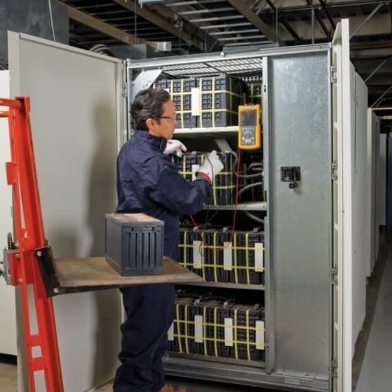 APC technician installing a Batt Manager main system module and fitting a tab washer inside a rack enclosure